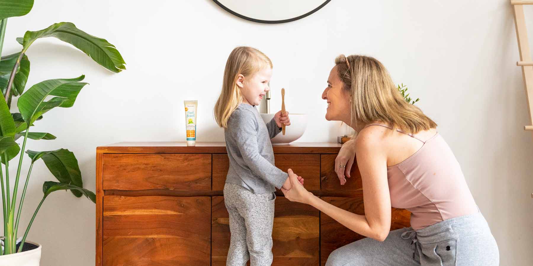 woman holding her daughter's hand smiling while they smile at each other during their morning dental routine