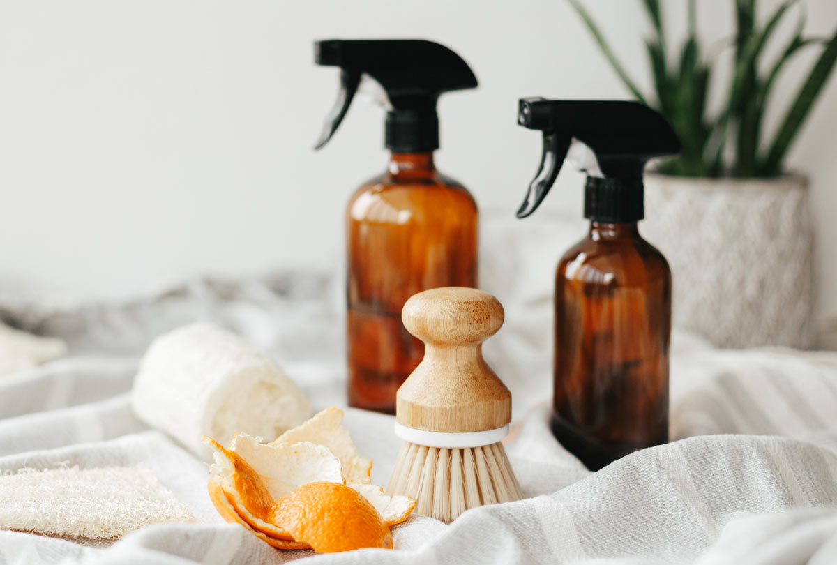latest-trends-in-home-deodorizers two glass spray bottles with a scrubby brush and orange peel