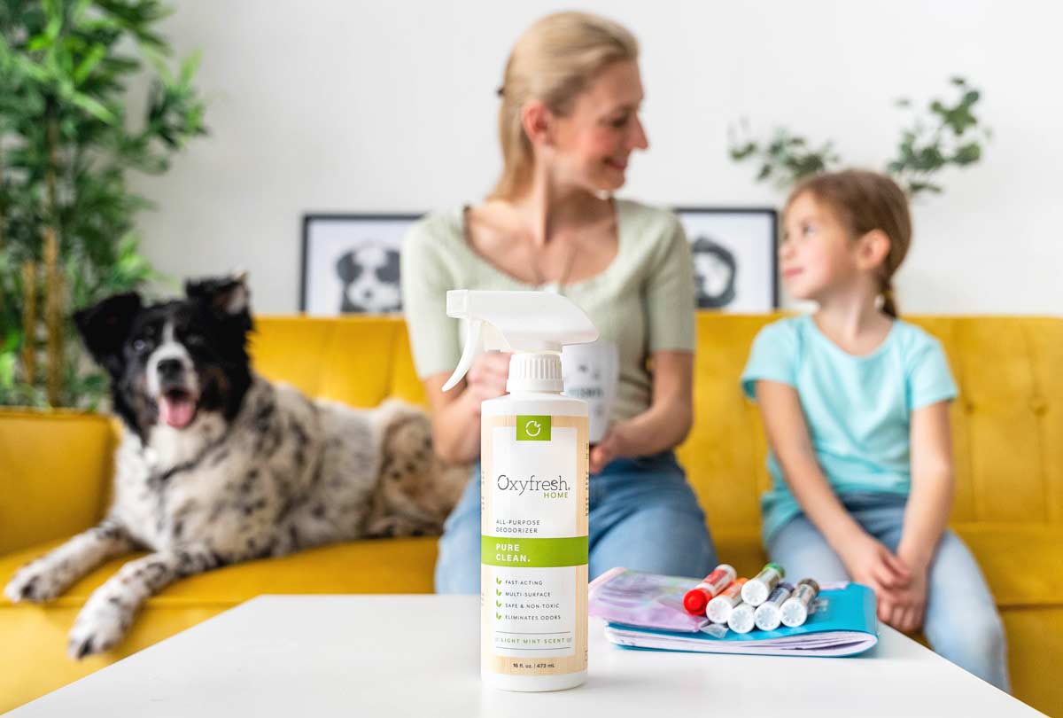 oxyfresh-all-purpose-deodorizer-on-the-table-in-front-of-mom-daughter-and-dog-sitting-on-a-bright-yellow-couch