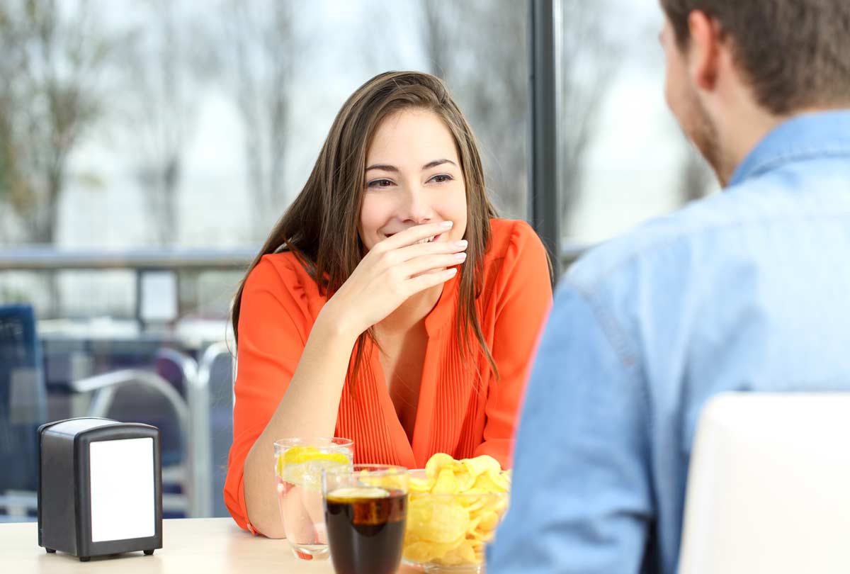 oxyfresh-dental-blog-titled-5-Secrets-to-Fix-Really-Bad-Breath-woman-smiling-covering-her-mouth-while-seated-at-a-table-on-a-date