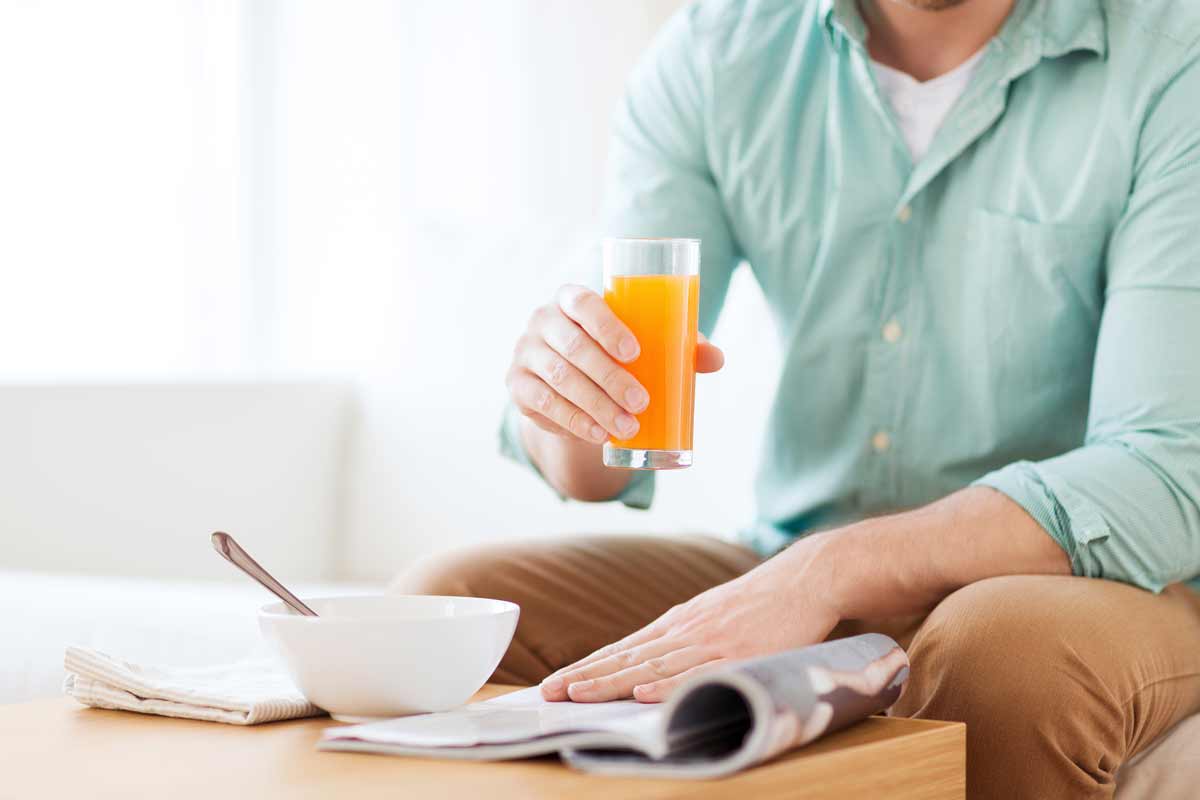 oxyfresh-dental-health-blog-image-of-man-sitting-on-the-couch-next-to-his-coffee-table-reading-a-magazine-and-holding-a-glass-of-orange-juice