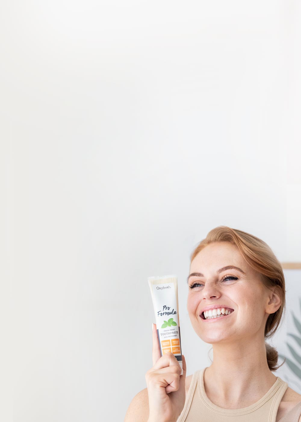 strawberry blond lady smiling brightly holding a tube of oxyfresh pro formula toothpaste which is gentle on her enamel to keep her teeth pearly white 