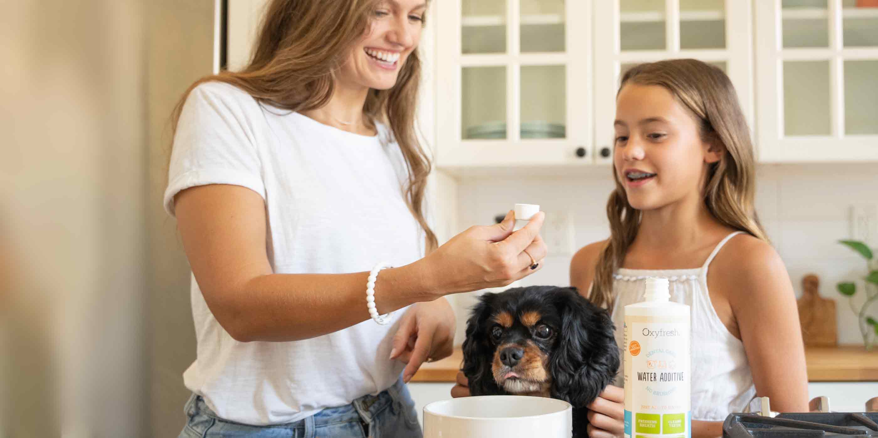 woman teaching her daughter how to keep good care of their pups teeth using oxyfresh pet water additive in a water bowl