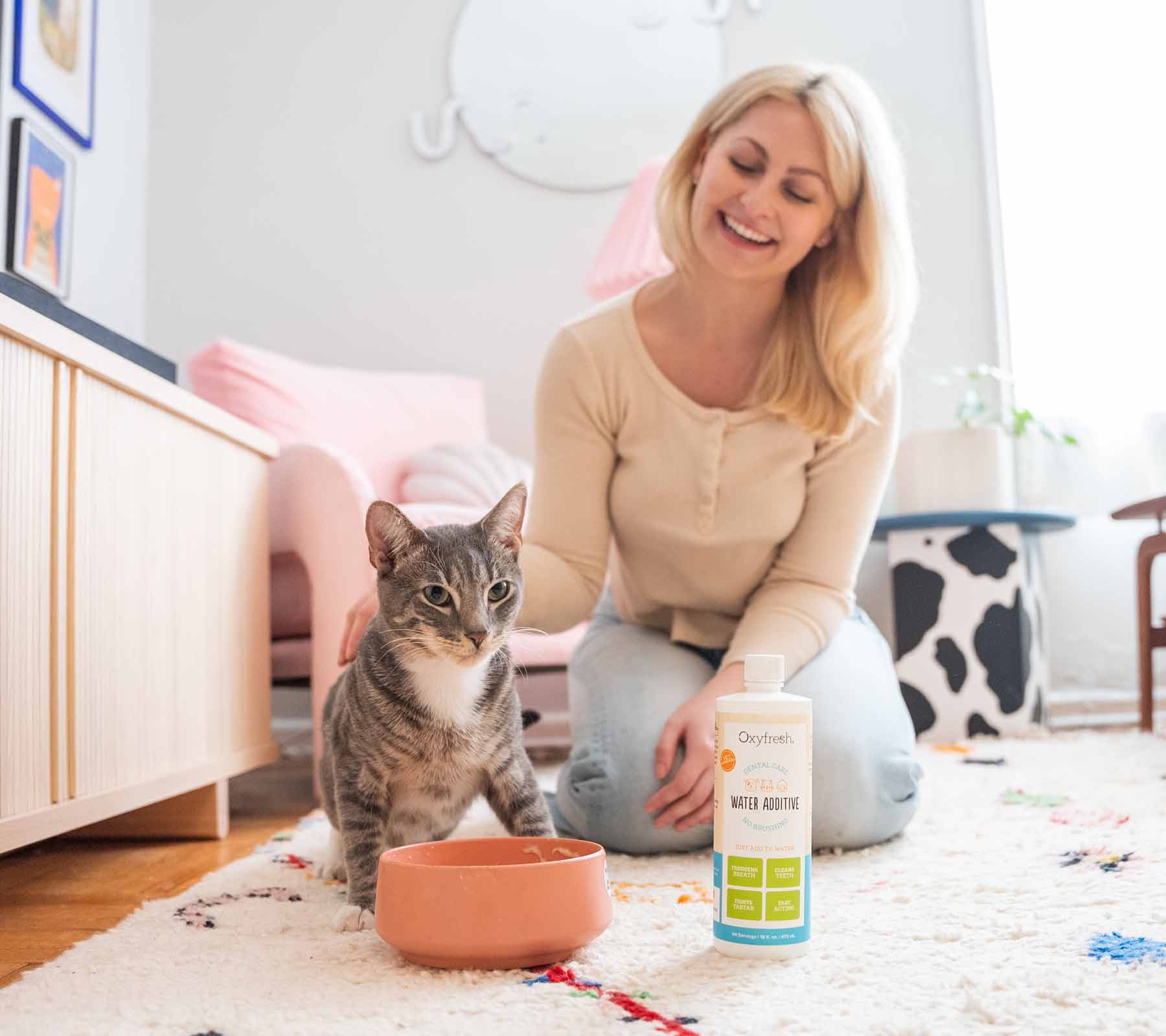 woman-smiling-petting-her-cat-in-the-living-room-next-to-oxyfresh-pet-water-additive-and-bowl