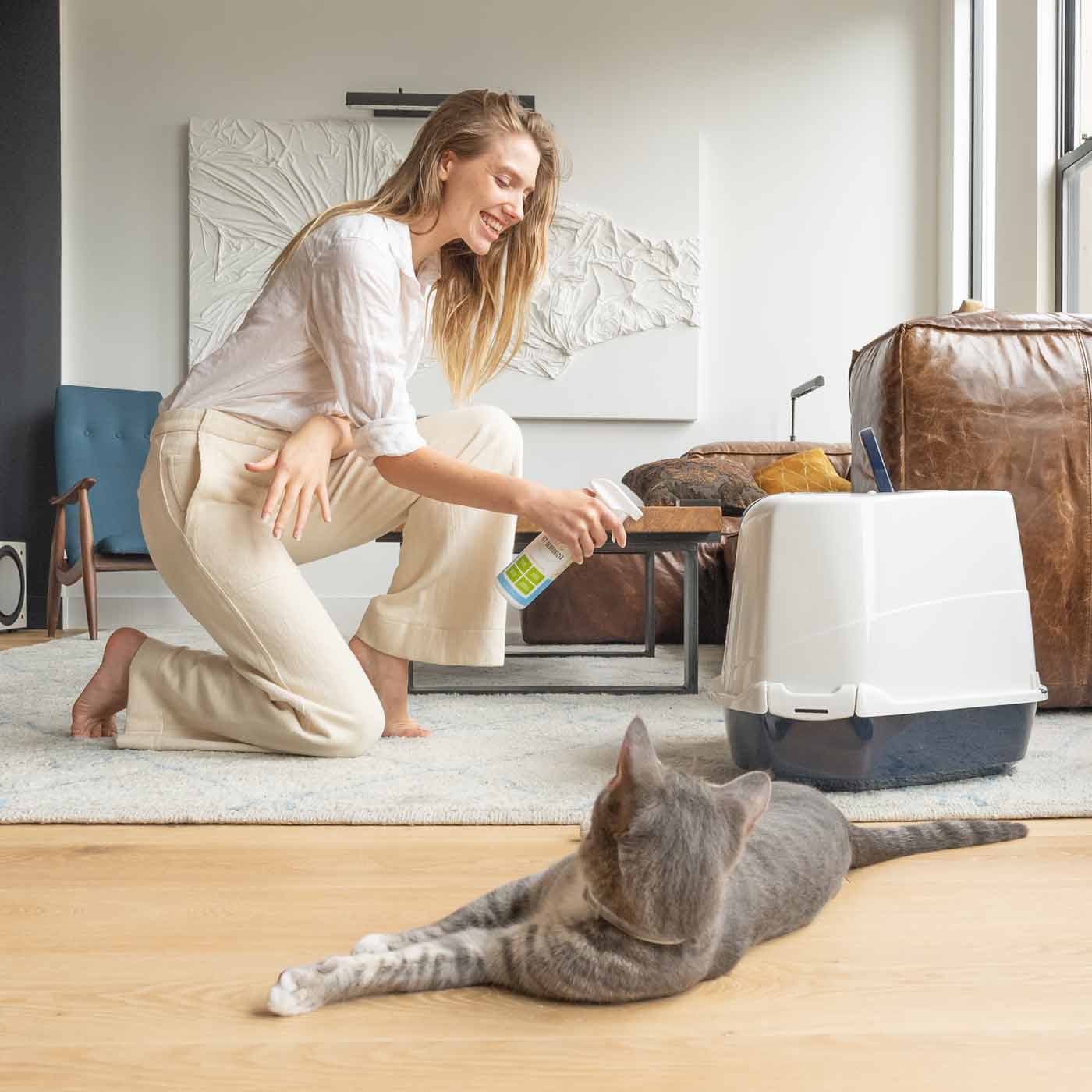 woman spraying litter box next to cat with oxyfresh pet deodorizer for any stinky space