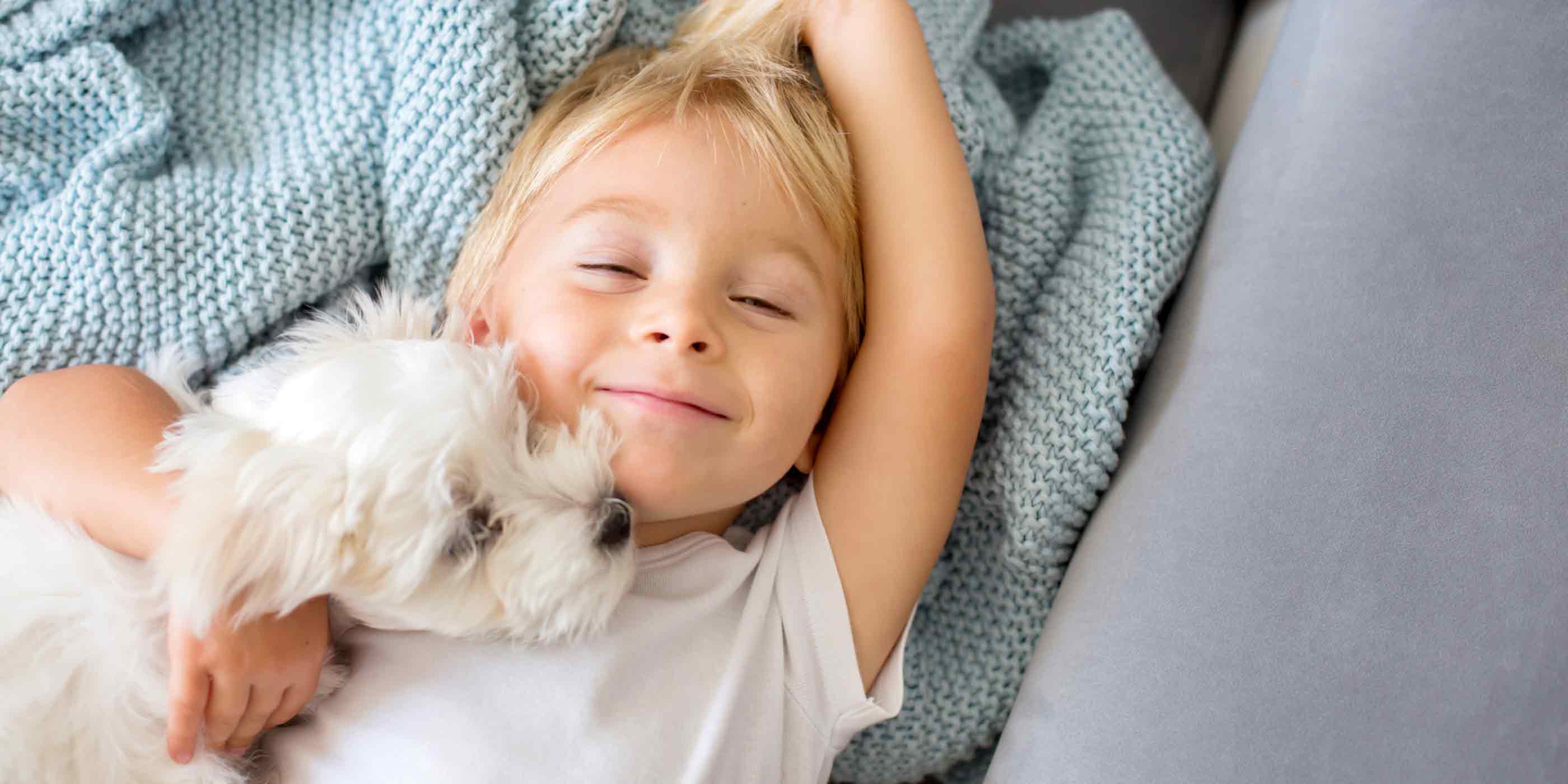 young-boy-smiling-sleepily-snuggling-with-his-cute-white-dog
