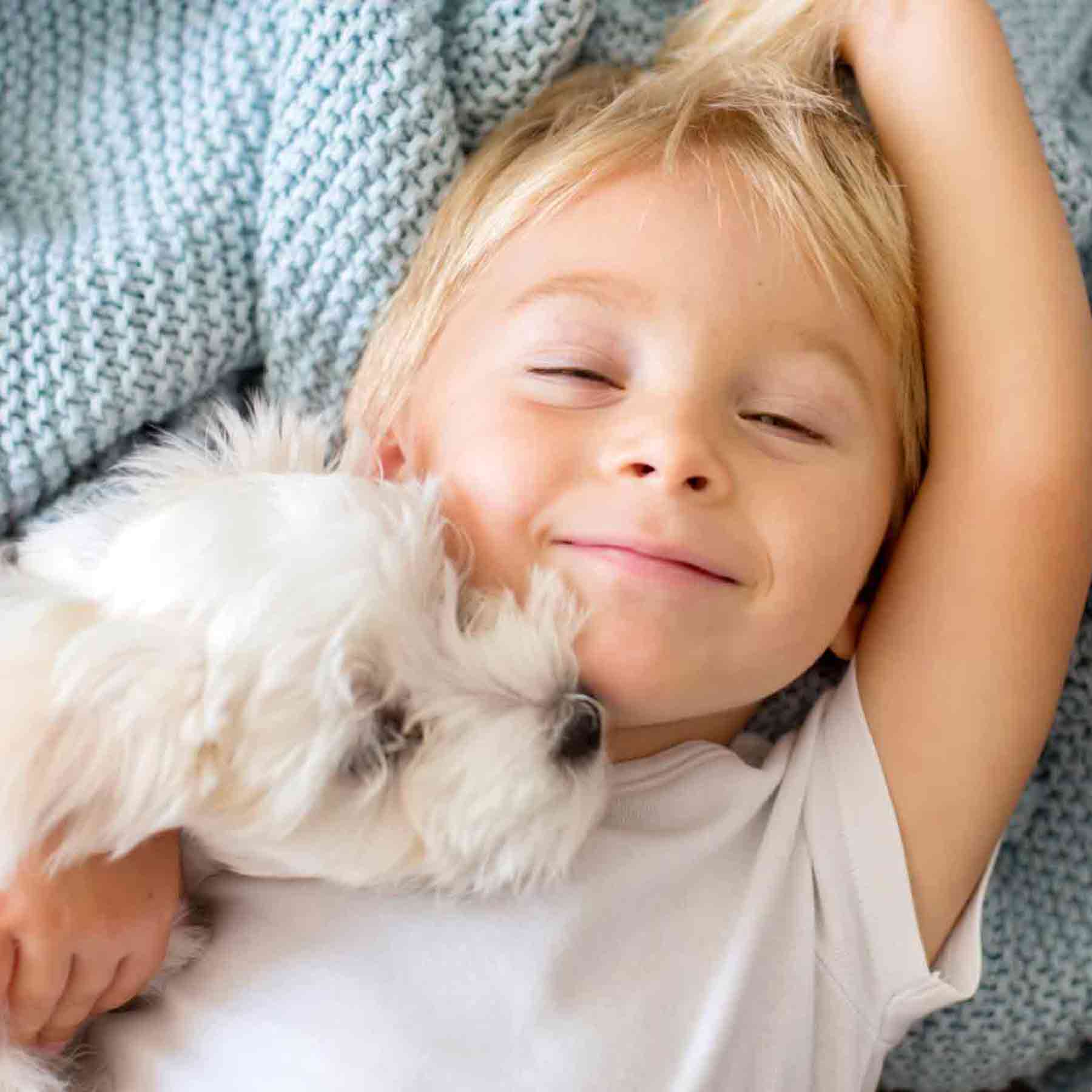 young-boy-smiling-sleepily-snuggling-with-his-cute-white-dog_mobile