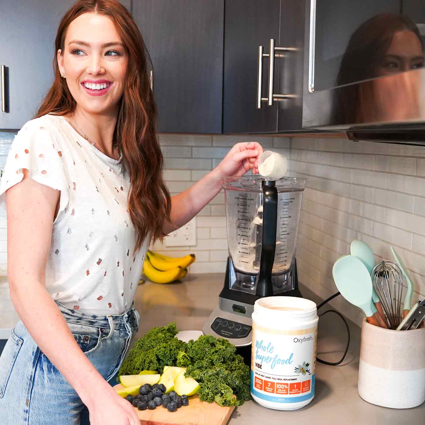 young-woman-smiling-over-her-shoulder-as-she-pours-oxyfresh-vibe-vanilla-vegan-and-dairy-free-protein-powder-into-blender_